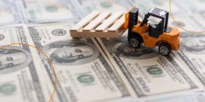 A toy excavator moves a pallet over one hundred dollar bills