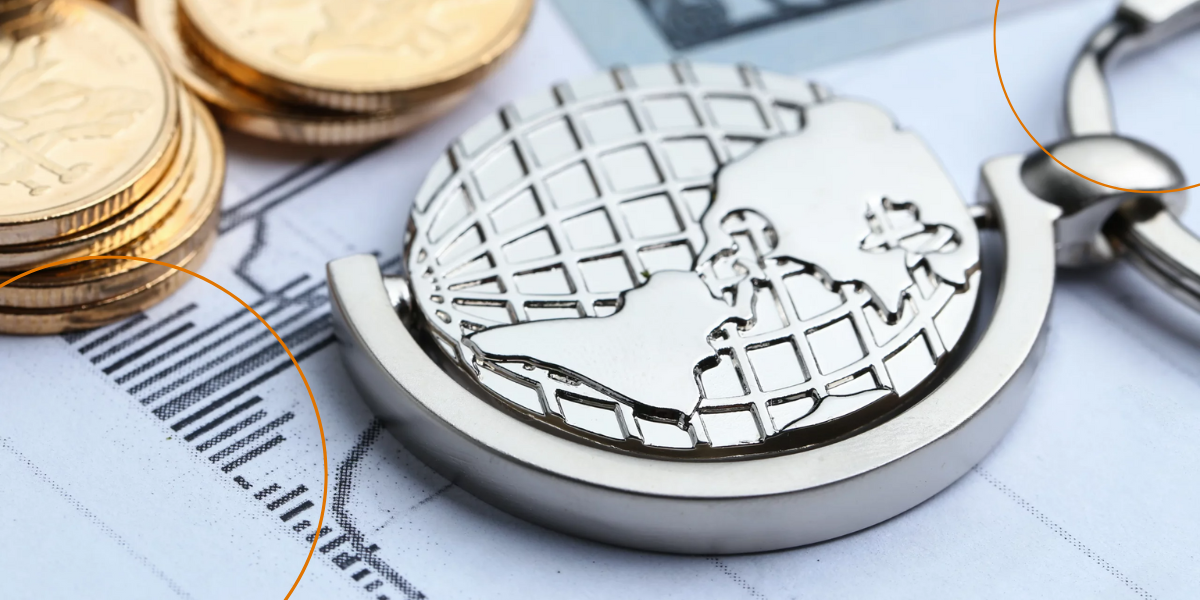 A silver globe key chain next to gold coins