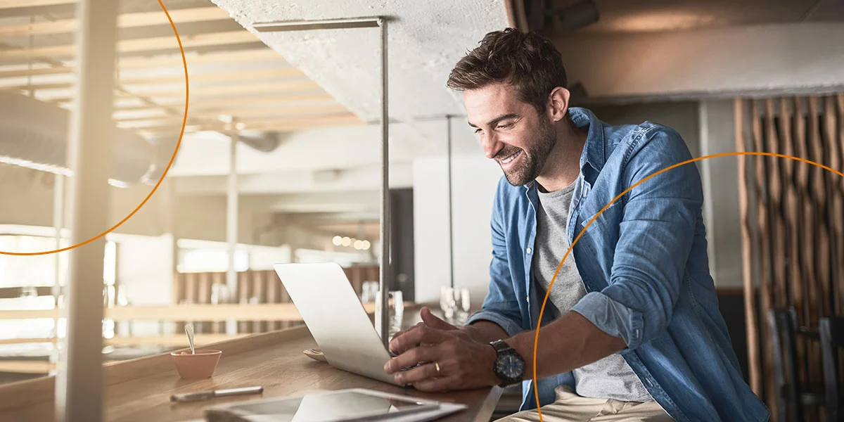 A man with brown hair smiles while looking at a laptop