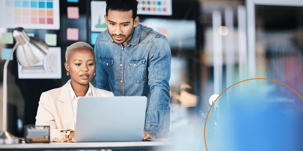 A woman shows a man her work on a laptop