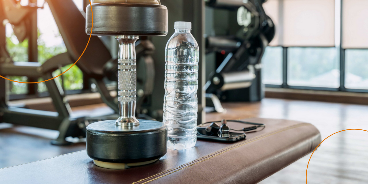 A dumbbell sits on a bench next to a water bottle, phone, and earbuds