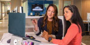 Two businesswomen review a desktop screen together