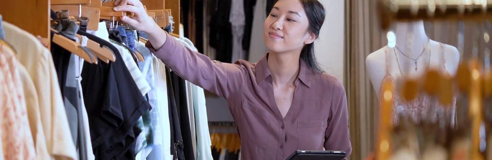 A retailer counts hangers while holding a tablet